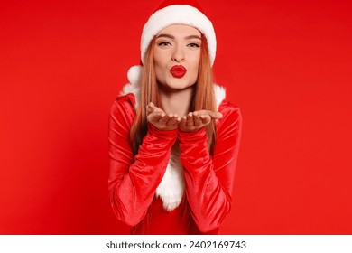 Young woman in Santa hat blowing kiss on red background. Christmas celebration - Powered by Shutterstock