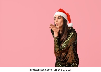 Young woman in Santa hat blowing kiss on pink background - Powered by Shutterstock