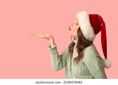 Young woman in Santa hat blowing kiss on pink background - Powered by Shutterstock