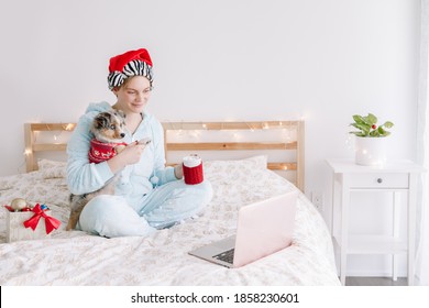 Young Woman In Santa Hat Hold Cute Puppy Dog And Call Friends Family. Pet Owner Celebrating Christmas Holiday Alone. Distant Remote Holiday Celebration Online On Internet. Coronavirus Lockdown.