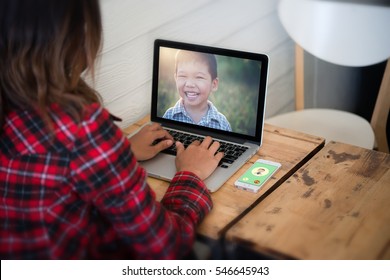 Young Woman Sat Looking Her Son Picture From Laptop While Relaxing At Home.