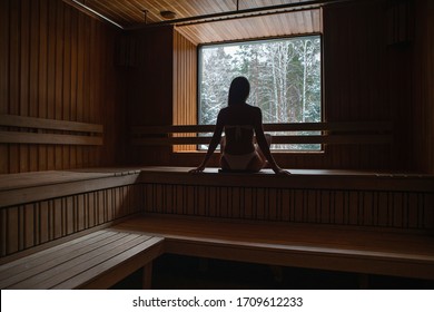 Young Woman In Sauna Room Watching Winter Forest Through The Window