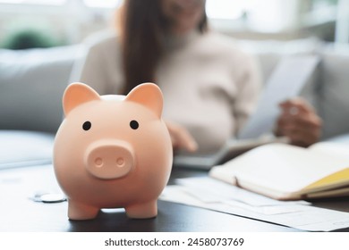 Young woman saving money monthly expenses putting coin in to piggy bank on the table. - Powered by Shutterstock