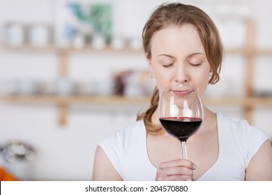 Young Woman Savoring The Bouquet Of A Glass Of Wine As She Sniffs At The Glass With Her Eyes Closed In Bliss As She Concentrates On The Smell, With Copyspace Indoors In The Kitchen