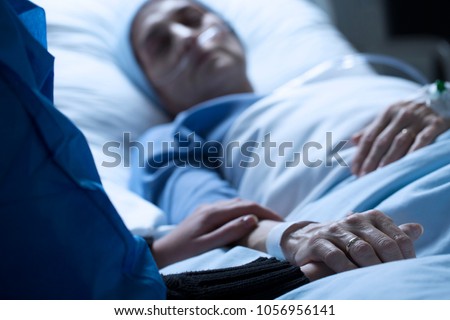 Young woman saying goodbye to her mother dying of cancer in a hospice, holding her hand