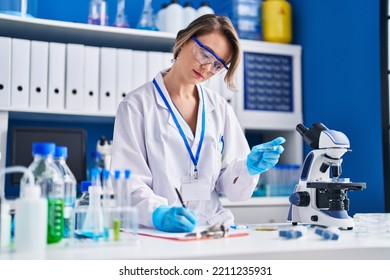 Young Woman Scientist Writing Report Holding Sample At Laboratory