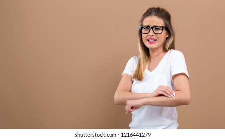 Young woman scratching her itchy arm. Skin problem. on a brown background