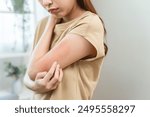 young woman scratching on her arm and has a red rash irritation on her skin from dust intolerance.