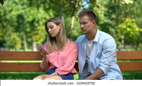 Young Woman Scrolling Phone Ignoring Hugging Man, Relationship Problems, Crisis