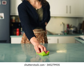 A Young Woman Is Scrubbing And Cleaning The Worktop In Her Kitchen With A Sponge