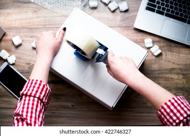 Young Woman Sealing A Box With Tape. Preparing For Moving. Packing, Selling Online, Shipping, Moving And Lifestyle Concept