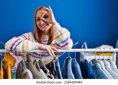 Young Woman Searching Clothes On Clothing Rack Smiling Happy Doing Ok Sign With Hand On Eye Looking Through Fingers 