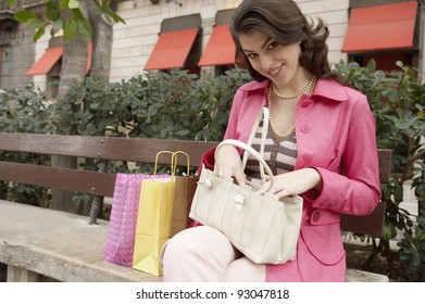 Young Woman Searching Through Her Purse While Sitting Down With Shopping Bags.