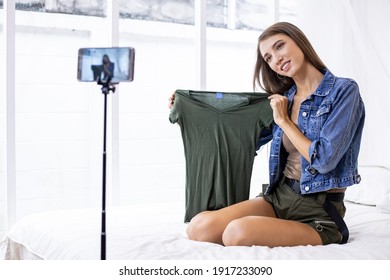 Young Woman Selling Clothes Online Via Her Mobile Phone On The Bed At Home. Sell Stuff Online. Live Selling.