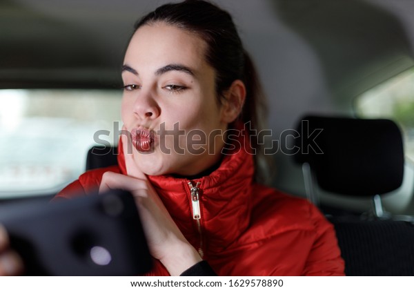 Young woman sending a kiss during a video call with a\
cell phone in a car