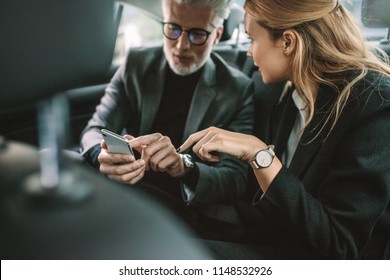 Young woman with senior businessman using mobile phone while traveling by a car. Business people using smart phone in taxi.