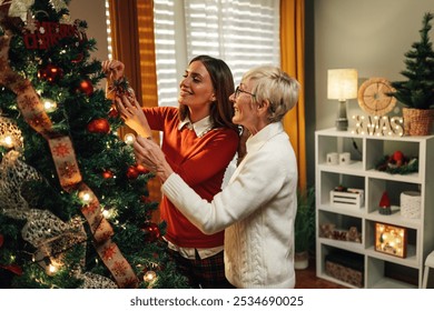 Young woman and a senior woman are decorating a christmas tree in a cozy home interior. They are smiling and having fun while preparing for the holiday season - Powered by Shutterstock