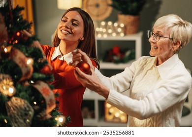 Young woman and a senior woman are decorating a christmas tree in their home, enjoying the festive atmosphere and each other's company - Powered by Shutterstock