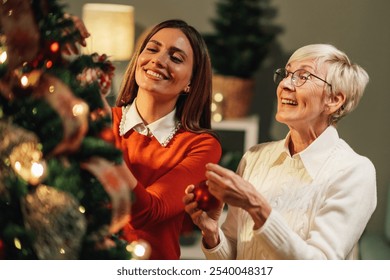 Young woman and a senior woman are decorating a christmas tree in their home. They are both smiling and happy to be spending time together during the holidays - Powered by Shutterstock