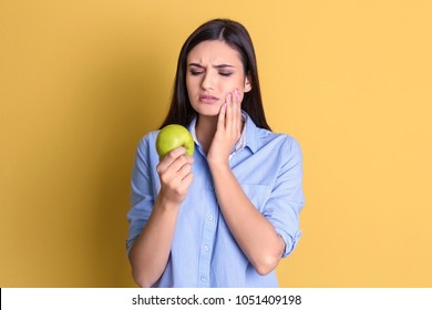 Young Woman With Sensitive Teeth And Apple On Color Background