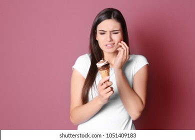 Young woman with sensitive teeth and cold ice cream on color background