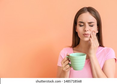 Young woman with sensitive teeth and cup of hot coffee on color background