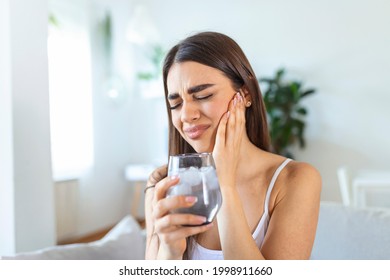 Young woman with sensitive teeth and hand holding glass of cold water with ice. Healthcare concept. woman drinking cold drink, glass full of ice cubes and feels toothache, pain
