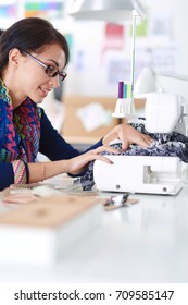 Young woman sewing while sitting at her working place .