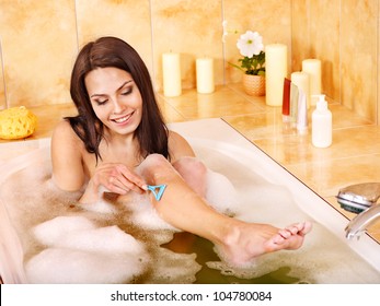 Young woman shaving her legs in  bath.
