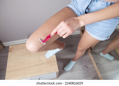  Young woman shaving her legs at room.