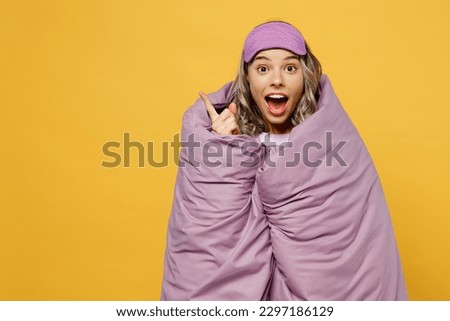 Young woman she wear pyjamas jam sleep eye mask wrapped in duvet blanket point aside above on area rest relax at home isolated on plain yellow background studio portrait. Good mood night nap concept