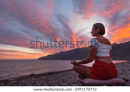 Young woman shilhouette in meditation position on the beach against sunset sky