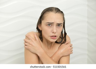 Young woman shivering with cold in the shower, the water is turned off, embracing her shoulders. Beauty concept photo
