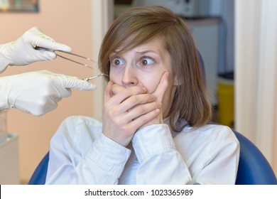 A Young Woman Is Shocked By The Fear And Horror Of Dental Instruments That She Looks At With Her Eyes Wide Open. The Concept Of Fear Of The Dentist And Dental Treatment