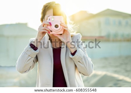 Young woman shooting with pink instant camera - Trendy girl taking snapshots outdoor with back sun light - New generation trends concept - Focus on shutter hands - Warm filter