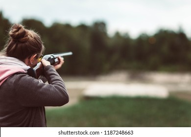 young woman shooting shotgun at clay pigeon outdoors with safety gear