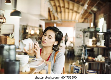 Young woman in a shop, looking at a ceramic jug - Shutterstock ID 604758590