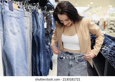 Mujer joven shopaholic eligiendo jeans en tienda de lujo, mujer prueba en pantalones a la venta grande en tienda