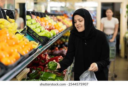 Young woman shopper in hijab buys bell peppers in grocery store - Powered by Shutterstock