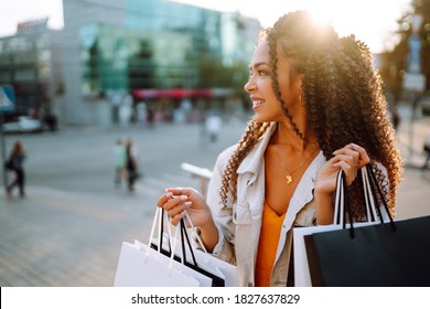 Young Woman With Shopping Bags Walking On Street. Fashionable African American Model Carrying Shopping Bags On Road. Purchases, Black Friday, Discounts, Sale Concept.