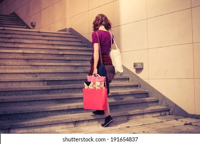A young woman with shopping bags is walking up the stairs outside at sunset