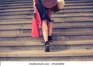 A Young Woman With Shopping Bags Is Walking Up The Stairs Outside At Sunset