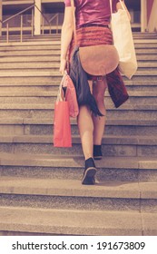 A Young Woman With Shopping Bags Is Walking Up The Stairs Outside At Sunset