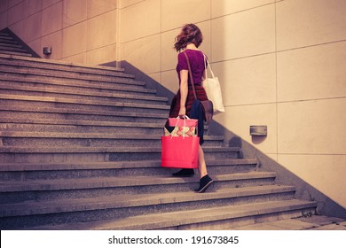 A Young Woman With Shopping Bags Is Walking Up The Stairs Outside At Sunset