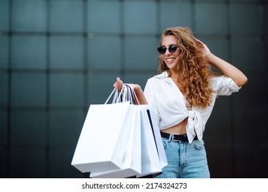 Young woman with shopping bags walking on street. Summer shopping. Consumerism, sale, purchases, shopping, lifestyle concept.