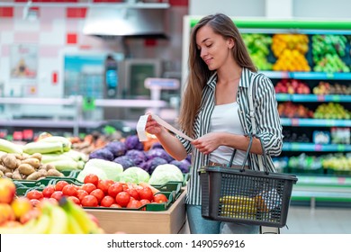 Young woman with shopping basket checks and examines a sales receipt after purchasing food in a grocery store. Customer buying products at supermarket 