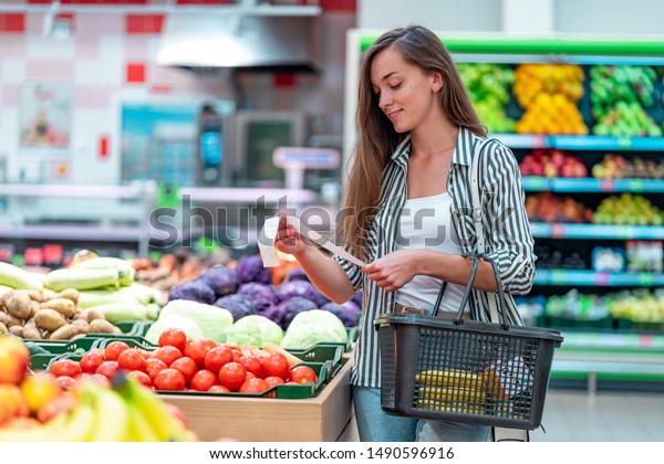 Young woman with shopping basket checks
and examines a sales receipt after purchasing food in a grocery
store. Customer buying products at supermarket
