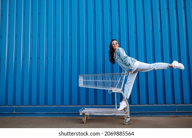 Young woman with shopping cart having fun near color wall. smilling african woman going shopping. Black friday. Consumerism, sale, discounts, lifestyle concept.