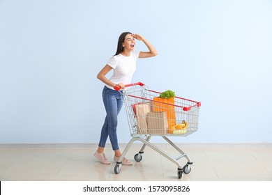 Young woman with shopping cart near color wall
