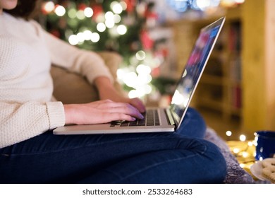 Young woman is shopping for Christmas gifts online using her laptop, sitting on the couch in living room with Christmas decorations. - Powered by Shutterstock